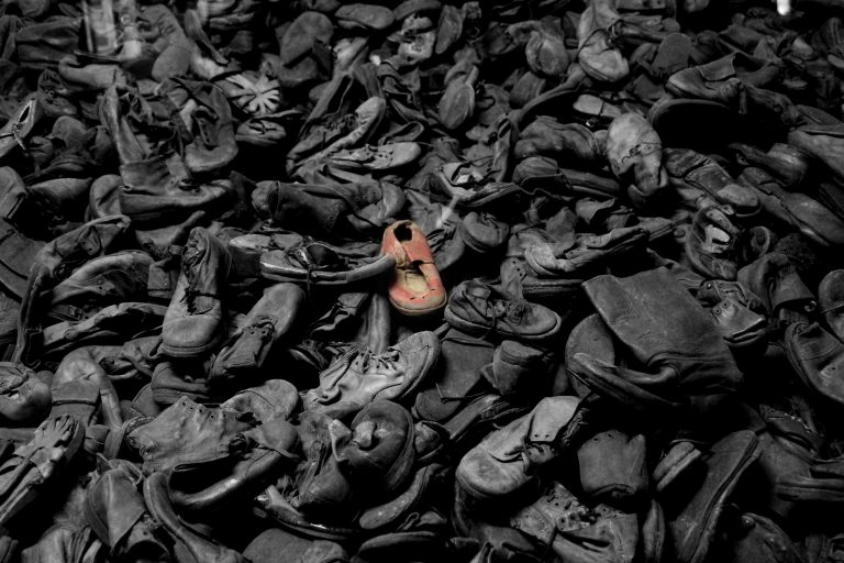 A pile of old children's shoes. The photo is black and white, but one show in the center is picked out in red.